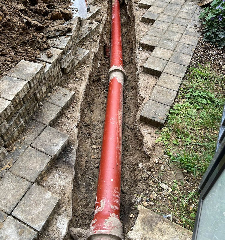 Tranchée ouverte dans une allée pavée, nouvelle canalisation d’eaux pluviales posée au fond