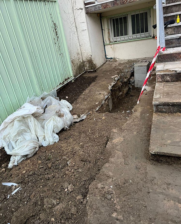 Tranchée ouverte le long d’une façade, regard en béton au bout du passage