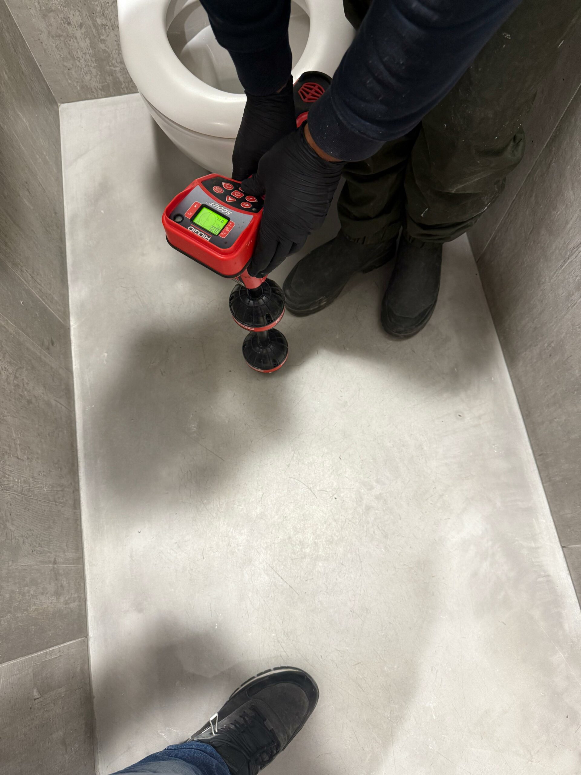 Technicien A.T.C. BAT en recherche de fuite, détecteur passé au sol des toilettes