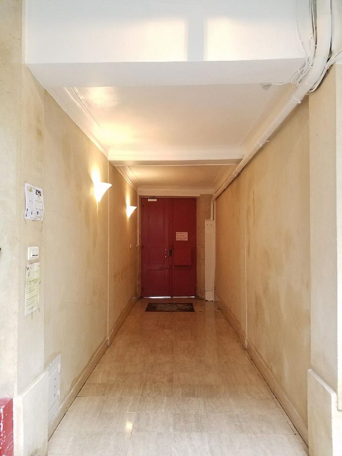 Hall d’immeuble après rénovation du plafond, porte rouge au fond